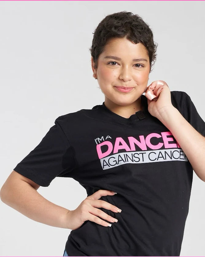 A young dancer in an I'm a Dancer Against Cancer tee, holding a pink awareness ribbon