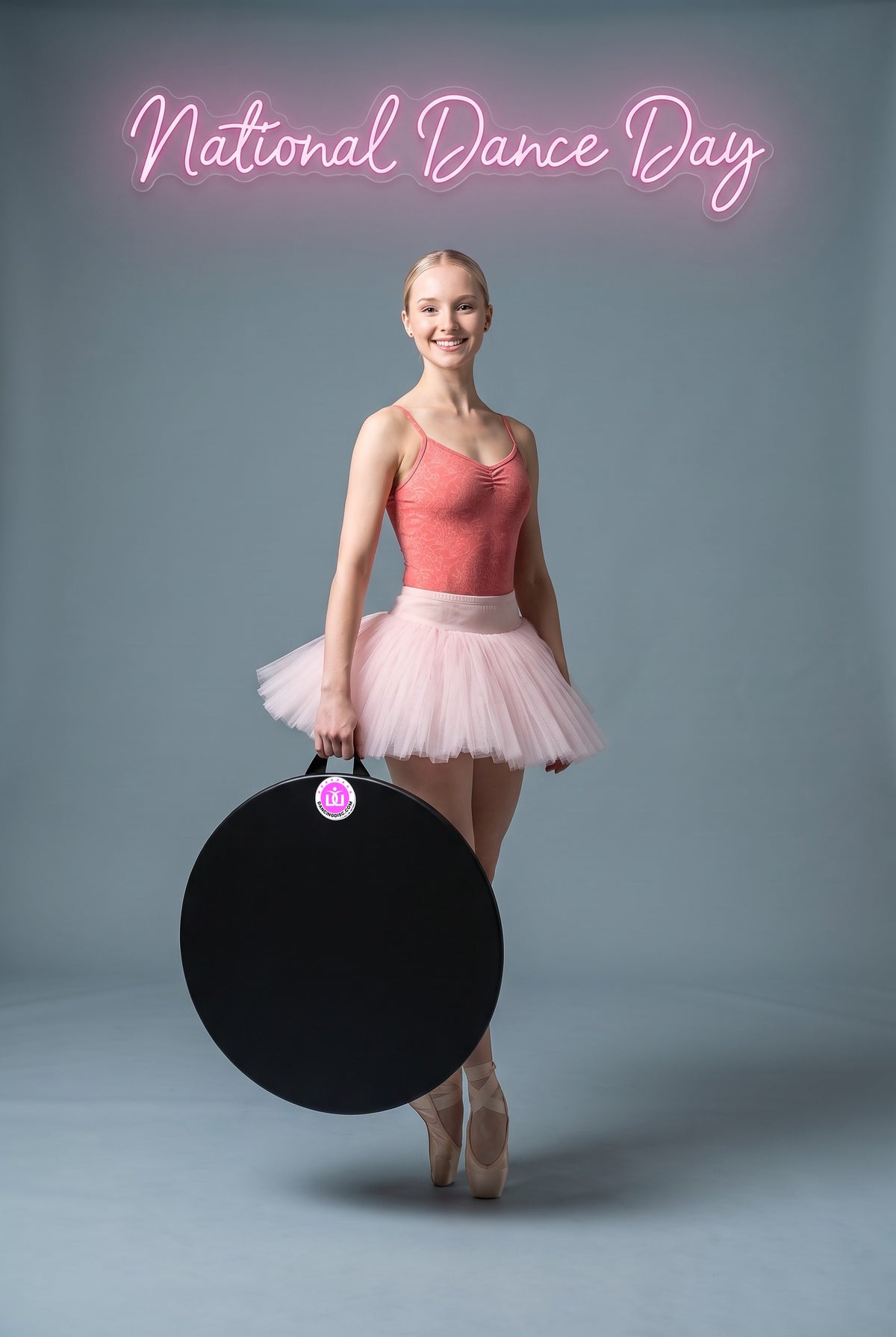A young dancer on pointe holding her 24-inch Dancing Disc under a neon sign that reads National Dance Day